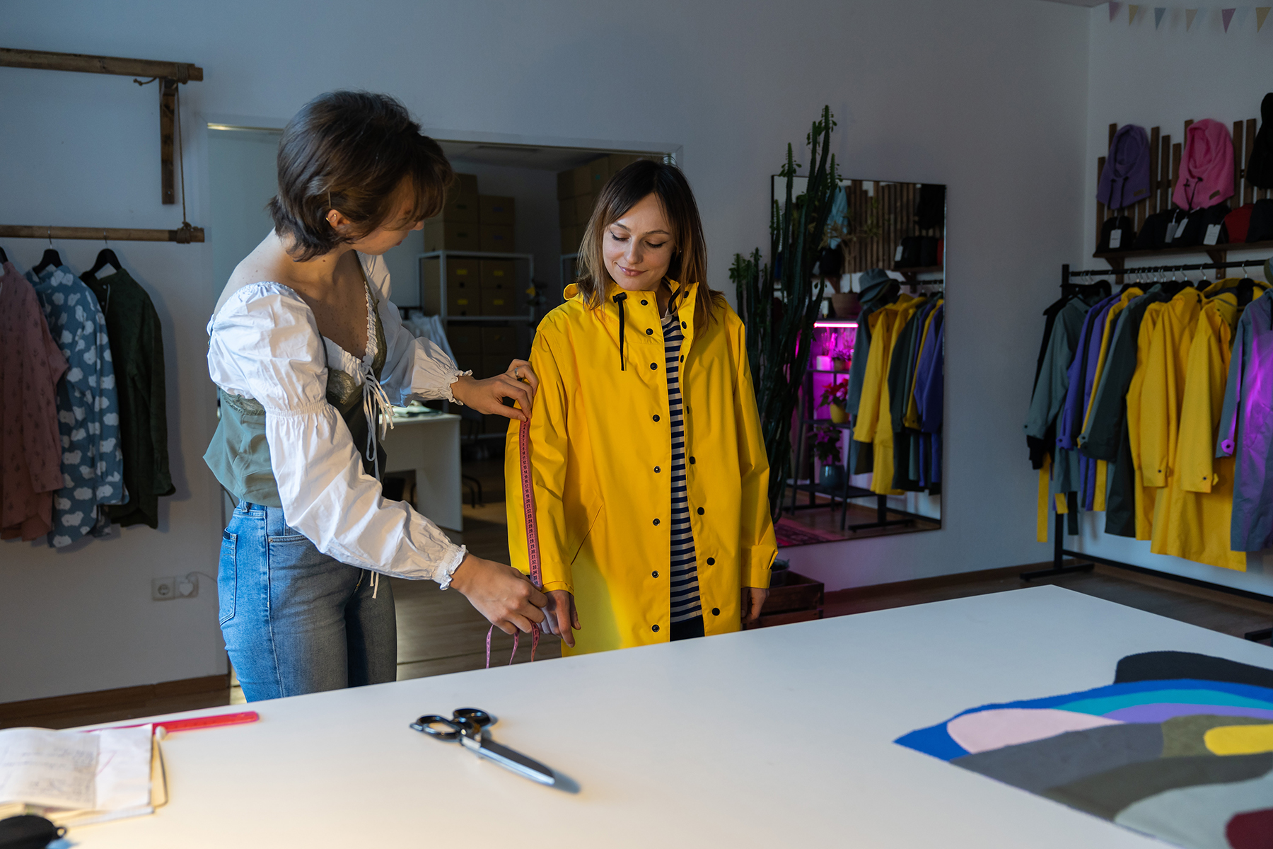 photo of fashion designer workshop with female tailor measuring and fitting bespoke yellow rain jacket.